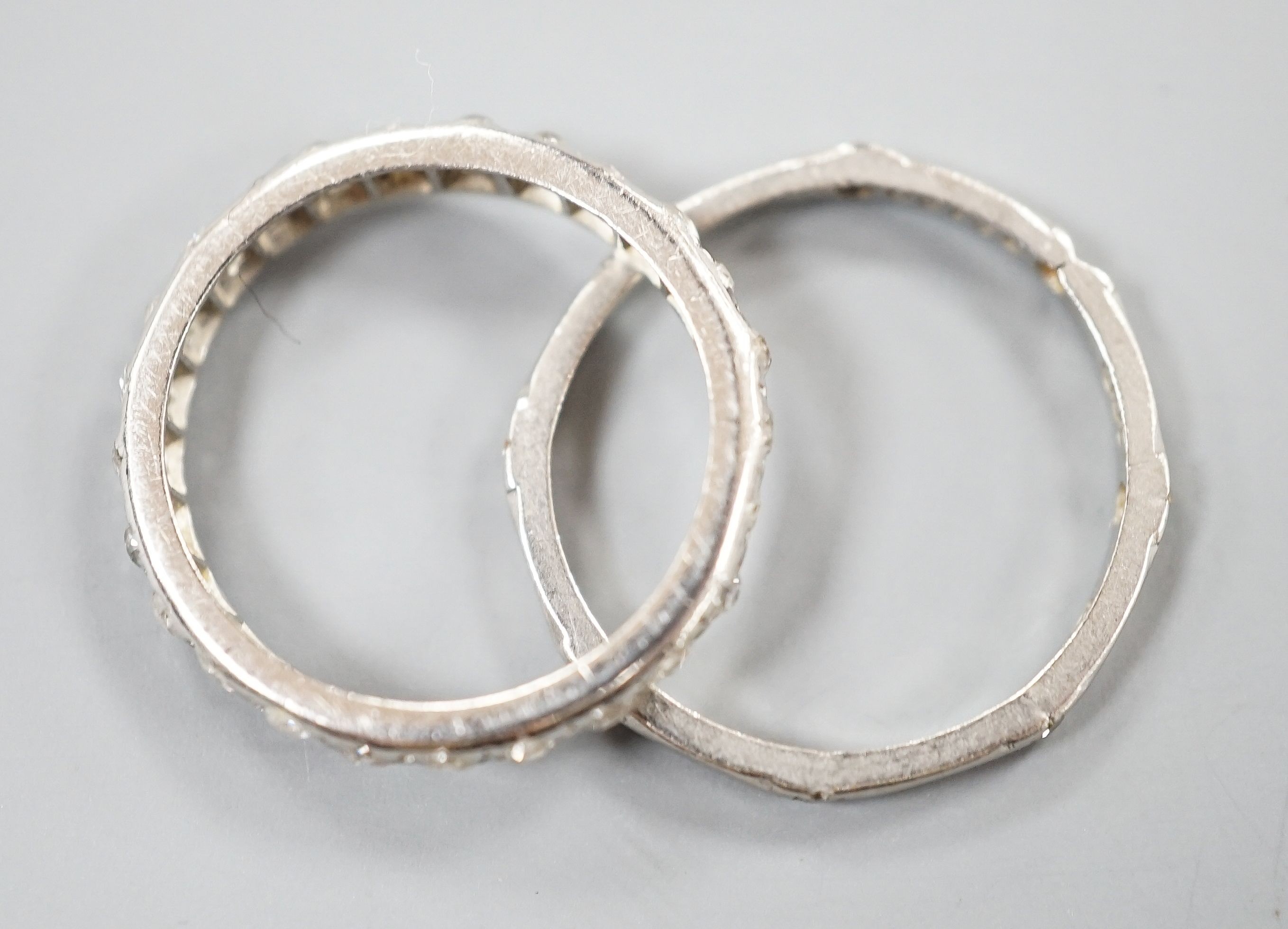 A white metal and diamond chip set full eternity ring, size J and a white metal (stamped Pt) and diamond set eternity ring (two stones missing), size L, gross weight 4.2 grams.